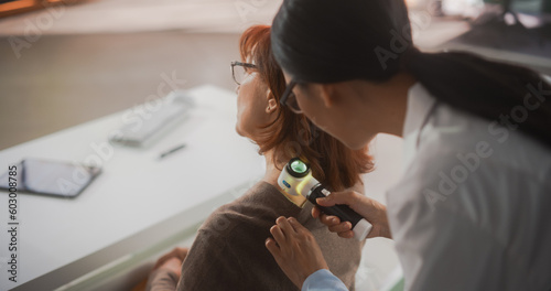 Young Asian Dermatologist is Using a Dermatoscope to Identify Worrying Cancerogenic Tissues on the Skin of a Senior Female During a Health Check Visit to a Clinic. Female Doctor Working in Hospital photo