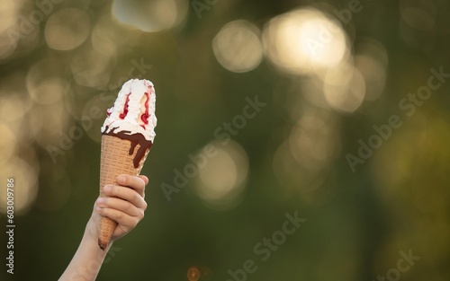 Children's hand holds ice cream in a cone on the background of nature. Summer vacation in the park.Sweets 