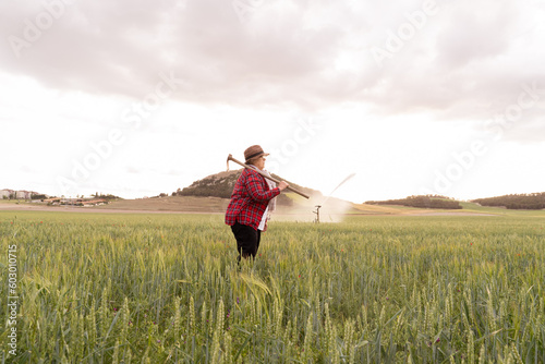 Caucasian grandmother wearing a straw hat holds her hoe over her shoulder to work in the crop fields stretching to the horizon.Backgrounds of grandparents working in the crop fields.