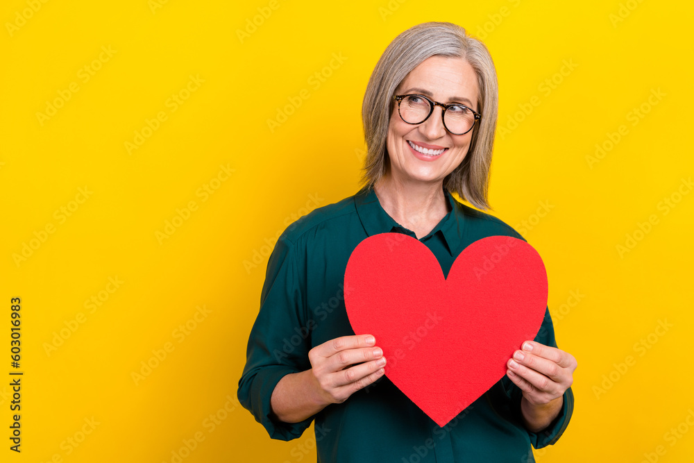 Photo of attractive positive lady hands hold heart card look empty space isolated on yellow color background Photo of attractive positive lady hands hold heart card look empty space isolated on yellow color background