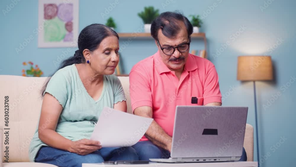 Indian senior couple discussing by checking documents or bills by using laptop at home - concept of technology, financial planning and relationship bonding