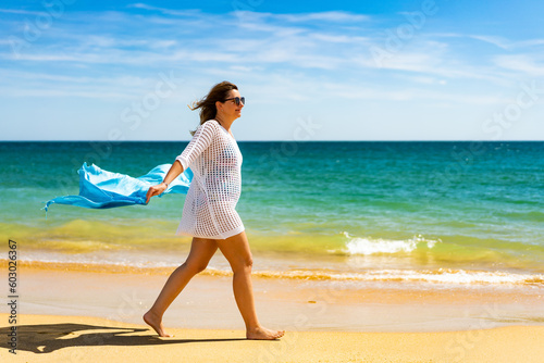 Beautiful woman walking on sunny beach holding shawl