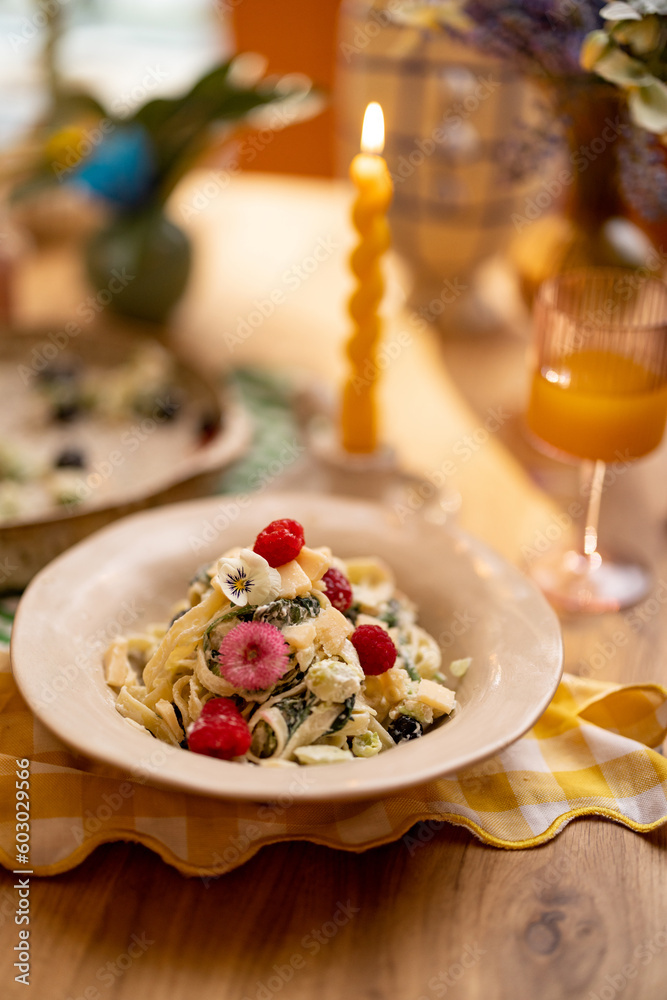 Tasty pasta with spinach and berries decorated with edible flowers on dining table Tasty pasta with spinach and berries decorated with edible flowers on dining table
