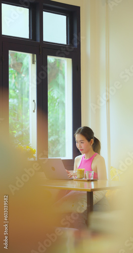 Beautiful Asian woman working in a cafe or restaurant alone. She uses the computer to work and search for information in restaurants.