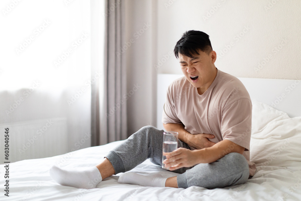 Chinese man sitting on bed, suffering from stomach pain Chinese man sitting on bed, suffering from stomach pain