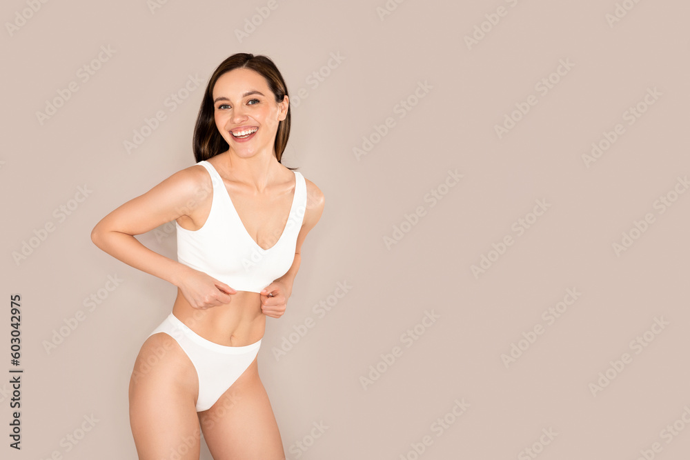 Naklejka premium Cheerful young woman in underwear smiling on beige background