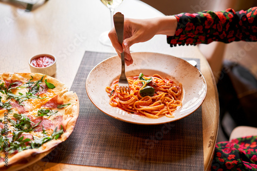 Italian Trattoria. Woman eats Italian pasta with tomato, meat. Spaghetti Bolognese wind it around a fork with a spoon. Parmesan cheese photo