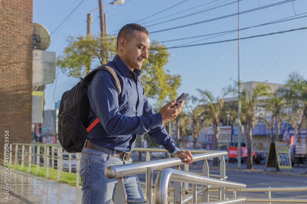 Young latin man with backpack looking at his mobile phone. Young latin man with backpack looking at his mobile phone.