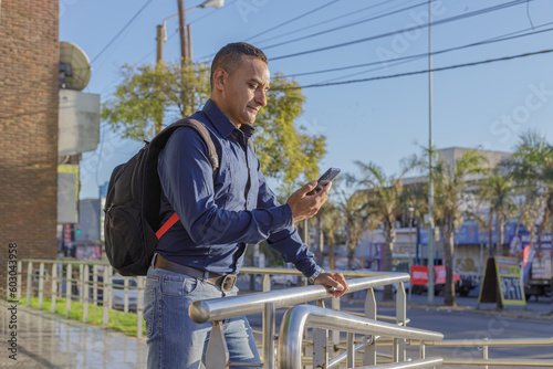 Young latin man with backpack looking at his mobile phone.