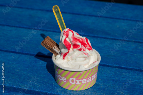 Tub of ice cream with flake and strawberry sauce in the sun