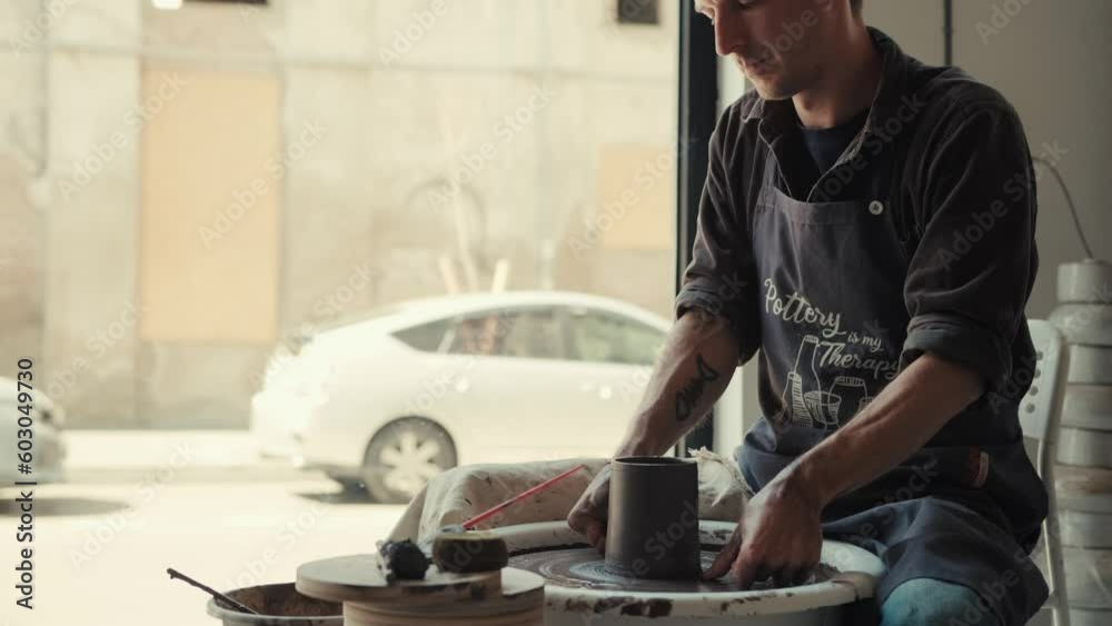 The potter works on the potter's wheel by the window. The process of making ceramic dishes from black clay.