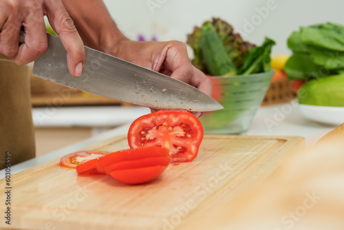 Close-up of asian male hand wearing apron I'm using a knife to slice tomatoes thinly. in the kitchen to prepare sandwiches for breakfast On days when working at home alone in the kitchen