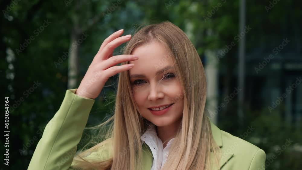 Portrait relaxed caucasian woman standing in city park looking at camera smiles, joyful blonde touching long hair with hand, elegant female wearing green jacket relaxing outdoors on summer day Portrait relaxed caucasian woman standing in city park looking at camera smiles, joyful blonde touching long hair with hand, elegant female wearing green jacket relaxing outdoors on summer day