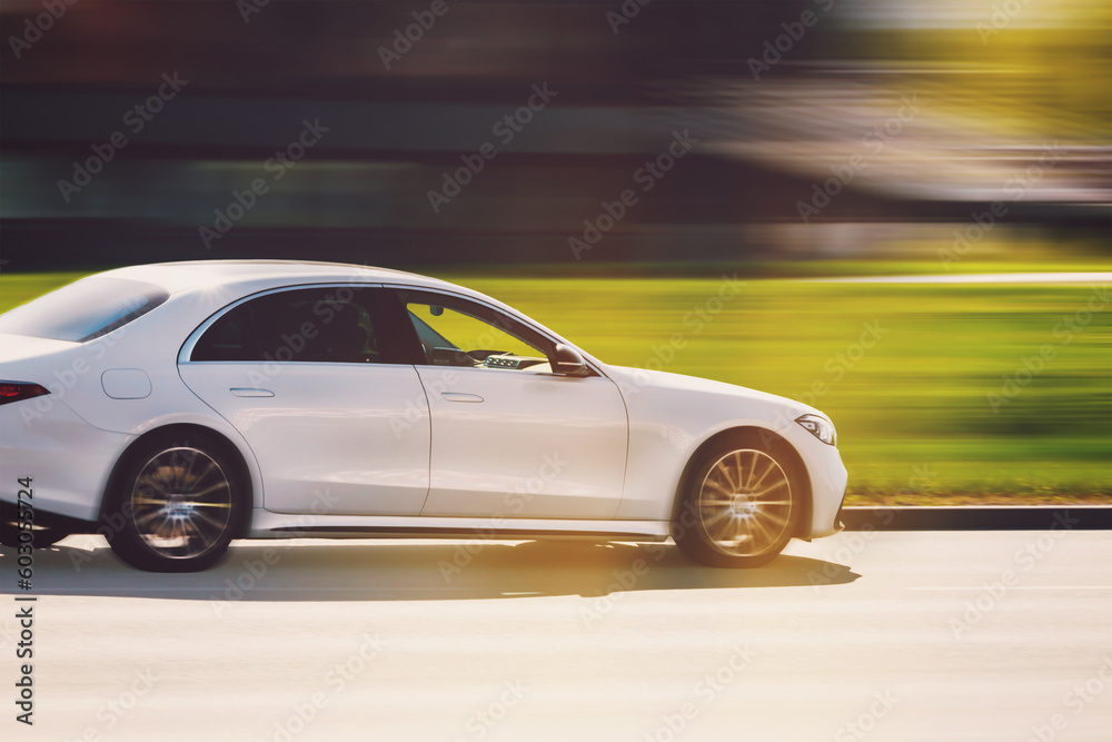 A white car is driving down the street at high speed. Large luxury sedan with motion blur background. Abstract photography of a fast moving blurred car on a speed blurred background