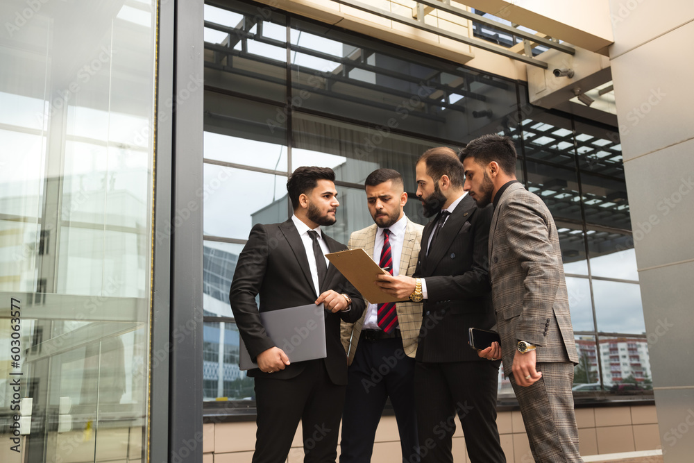 Business partners jointly discuss the difficulties and the implementation of ideas. Young successful men in suits at a team meeting outside the office Business partners jointly discuss the difficulties and the implementation of ideas. Young successful men in suits at a team meeting outside the office