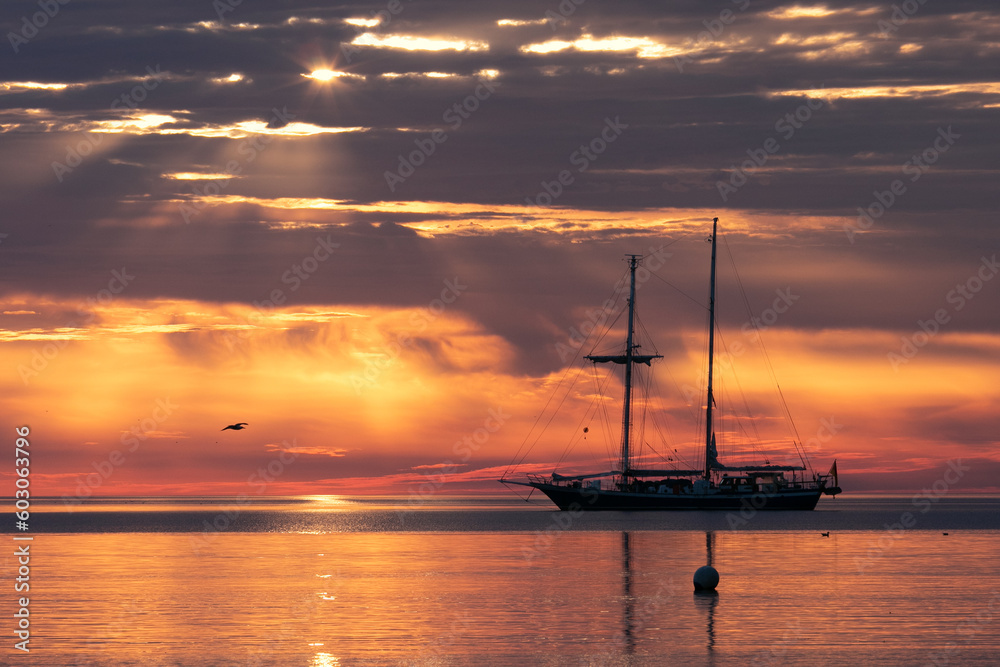 Silhouette of a traditional sailing ship with epic morning sky and dramatic sunrays. 