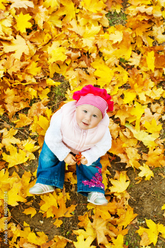 Baby sitting in autumn leaves and looking up
