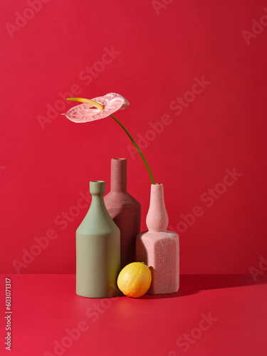 A pink flamingo-lily in a ceramic vase against a red wall