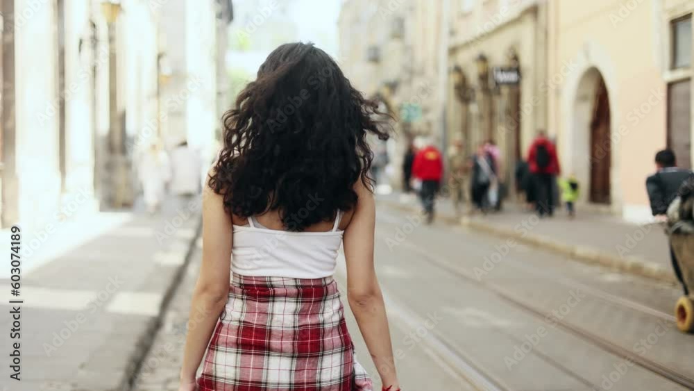 Charming young indian woman walking down the street turns around with flying hair and looking around outdoors Happy relaxed lady walking on the city centre enjoying beautiful day Charming young indian woman walking down the street turns around with flying hair and looking around outdoors Happy relaxed lady walking on the city centre enjoying beautiful day