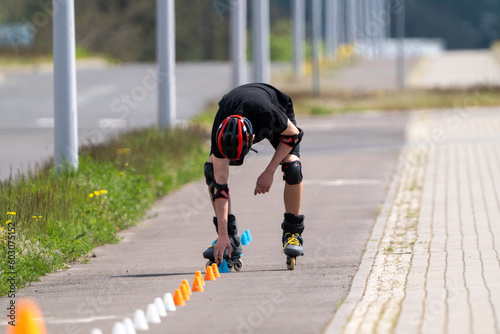 A boy in a black sweatshirt and helmet on roller skates is adjusting the cones on the slalom track by the street
