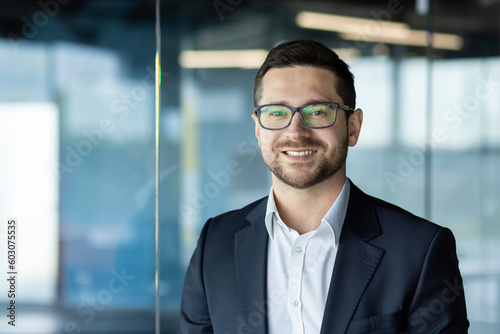 Close-up photo. Portrait of a young businessman, founder, director in a suit and glasses standing in the office and smiling at the camera photo