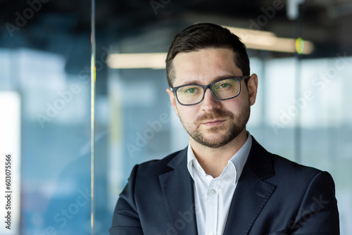 Close-up photo. Portrait of a successful young male teacher, business coach, personal growth trainer standing in the office and confidently and seriously looking at the camera