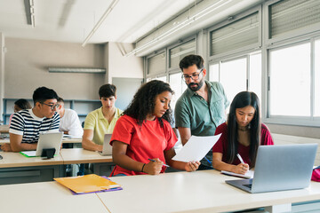 Young teacher explaining exercise to teenager girl students at High School Classroom