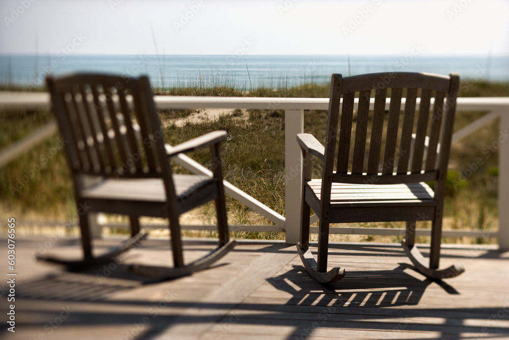 Two wooden rocking chairs sitting on a deck. They are facing the shore. Horizontal shot.