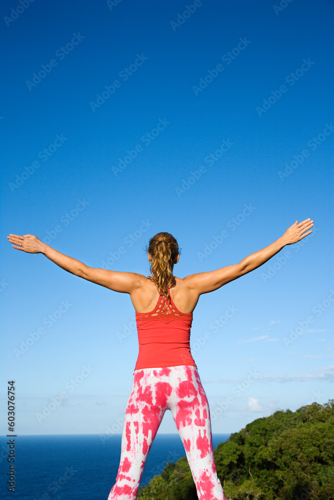 Attractive young woman stands with her arms spread open doing yoga on a deck. The ocean is in the background. Vertical shot. Attractive young woman stands with her arms spread open doing yoga on a deck. The ocean is in the background. Vertical shot.
