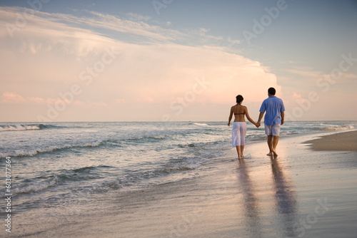 Rear view of a couple walking on the beach, holding hands. Horizontal shot.
