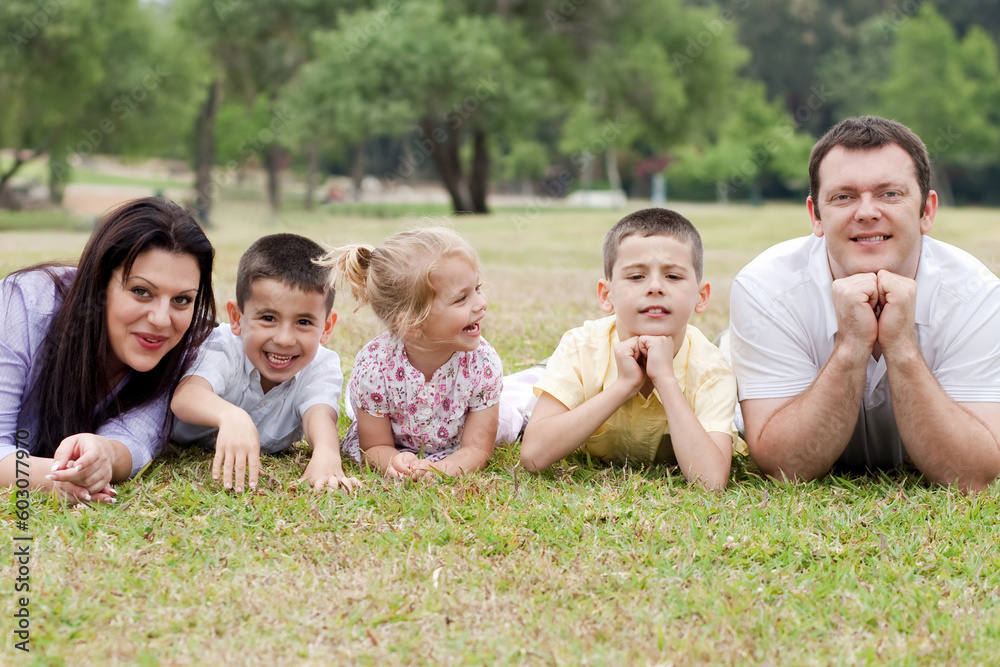 Cheerful family of five lying on lawn in the green park and looking at you Cheerful family of five lying on lawn in the green park and looking at you