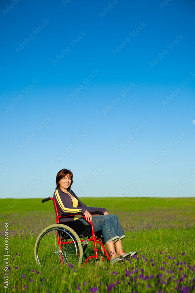 Handicapped woman on a wheelchair smiling over a green meadow Handicapped woman on a wheelchair smiling over a green meadow