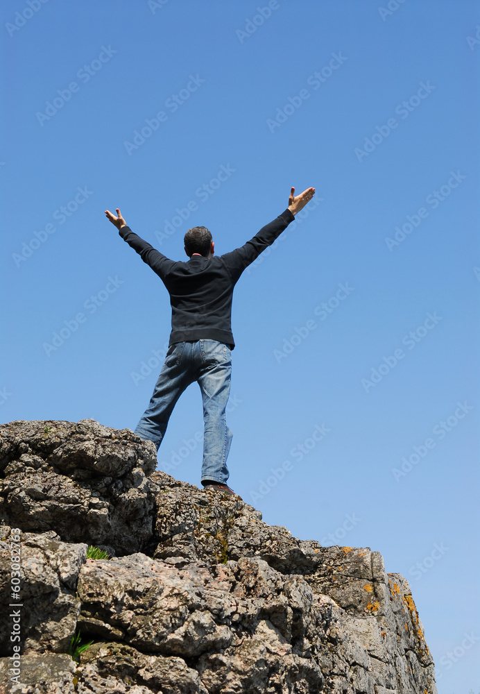 A man standing on a cliff with his arms raised to the blue sky A man standing on a cliff with his arms raised to the blue sky
