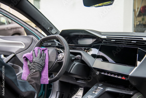 modern car dashboard is beeing carefully cleaned with a micro fiber towel from an professional car detailing service using gloves.. 