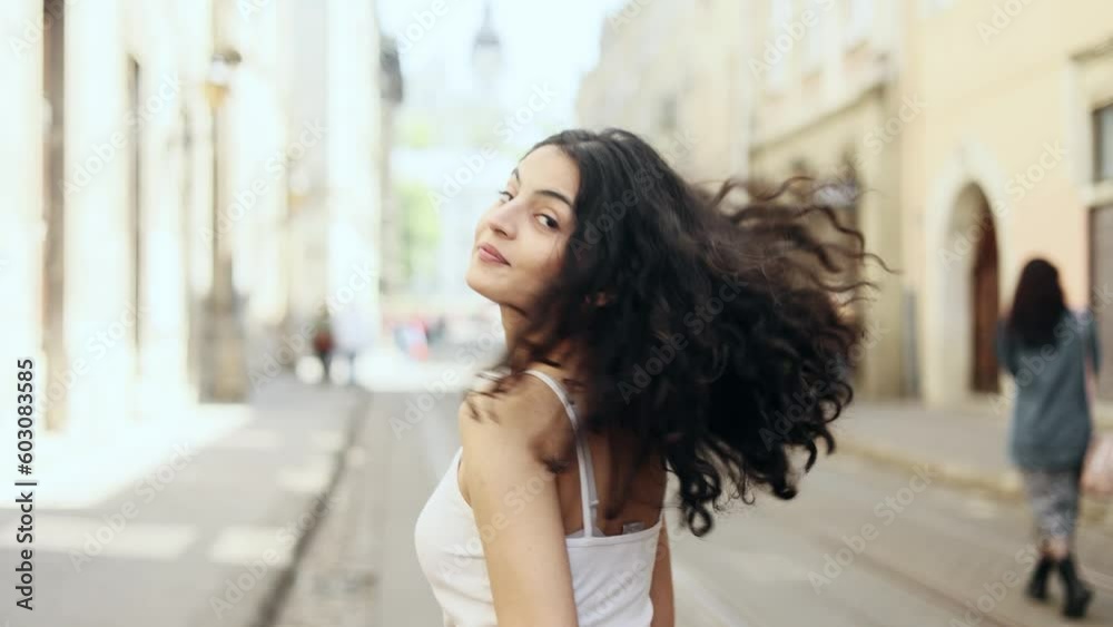Charming young indian woman walking down the street turns around with flying hair and looking at camera outdoors Happy relaxed lady walking on the city centre enjoying beautiful day Charming young indian woman walking down the street turns around with flying hair and looking at camera outdoors Happy relaxed lady walking on the city centre enjoying beautiful day