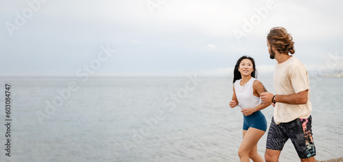 Cheerful young multi-ethnic couple running on the sandy sea beach wearing summer sport clothing