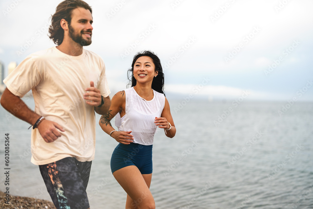 Cheerful young multi-ethnic couple running on the sandy sea beach wearing summer sport clothing Cheerful young multi-ethnic couple running on the sandy sea beach wearing summer sport clothing