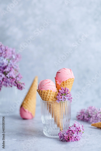 Vegan pink strawberry ice cream in cones with lilac flowers on a gray background. Healthy vegan dessert