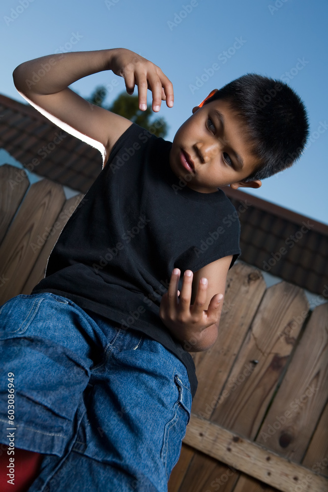 Young asian boy outside beside a tall wooden fence wearing jeans and black tshirt Young asian boy outside beside a tall wooden fence wearing jeans and black tshirt