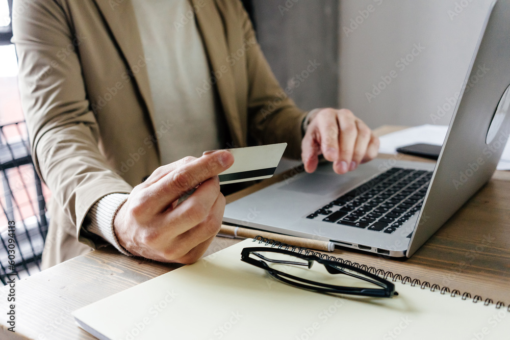 Anonymous man doing doing payment with card via laptop at table