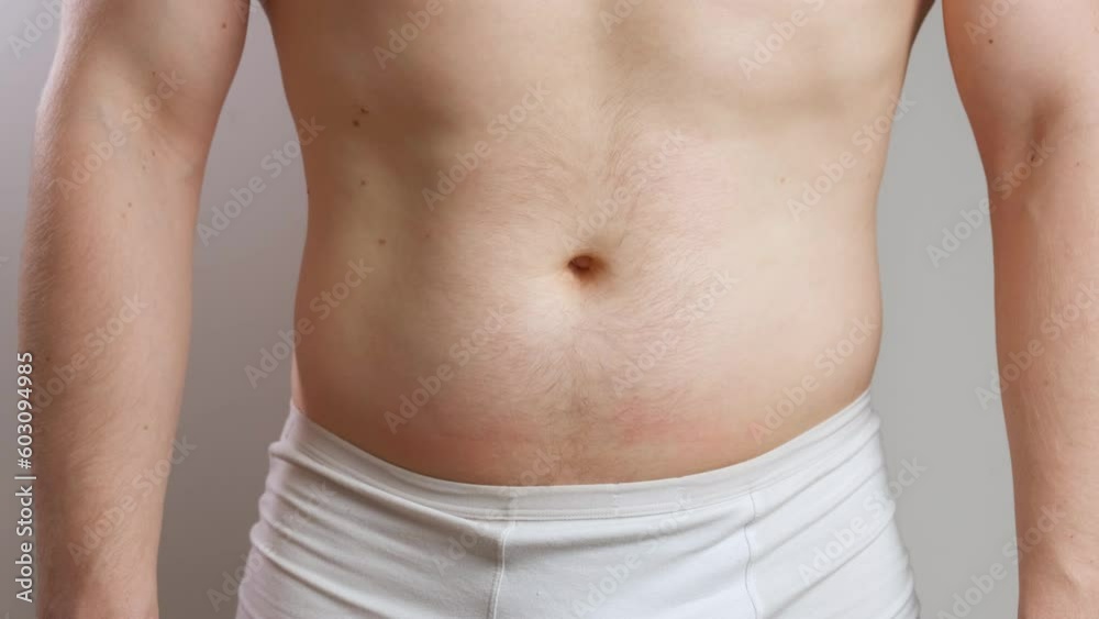 A man with a bare torso in white underpants pulls in a big belly and strains his abs in close-up. The concept of diet and weight loss. Front view A man with a bare torso in white underpants pulls in a big belly and strains his abs in close-up. The concept of diet and weight loss. Front view