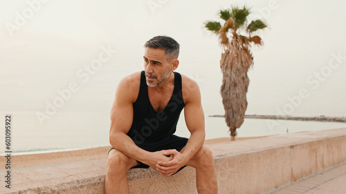 Middle-aged muscular man sitting on the promenade after jogging