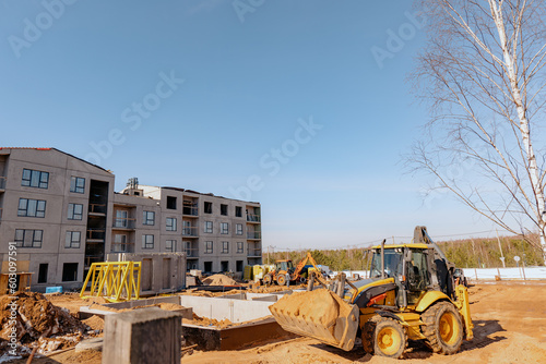 Tractor at the construction site. Excavator machine unloading sand during earth moving works. Panel building under construction.