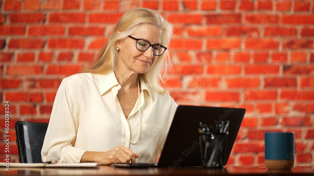 Middle age mature woman using laptop computer unable to see screen, puts glasses on and is happy with good vision. - obrazy, fototapety, plakaty 