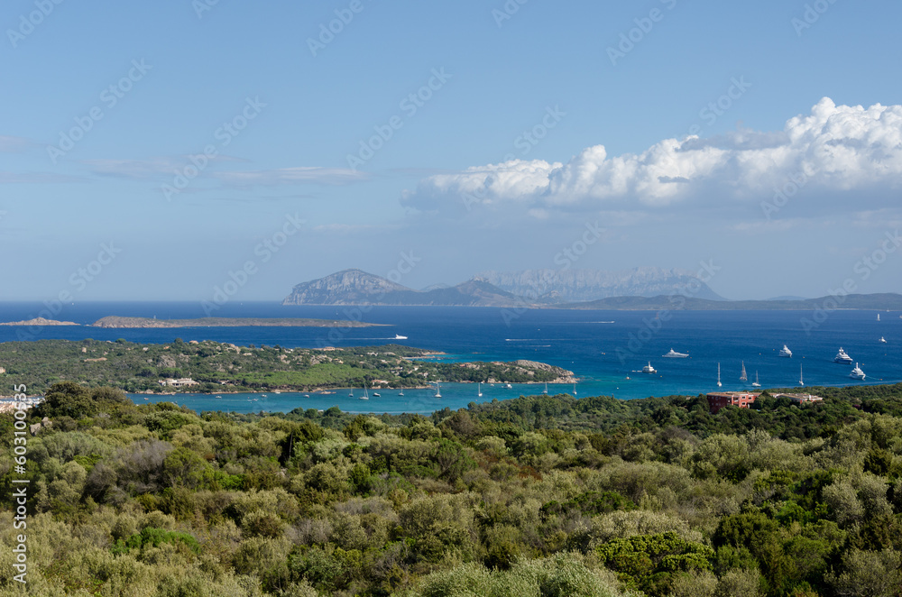 The wide-angle view of the Sardinian picturesque seacoast, blue waters with yachts and hills in the distance