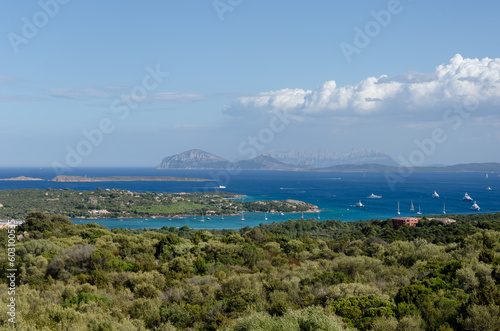 The wide-angle view of the Sardinian picturesque seacoast, blue waters with yachts and hills in the distance