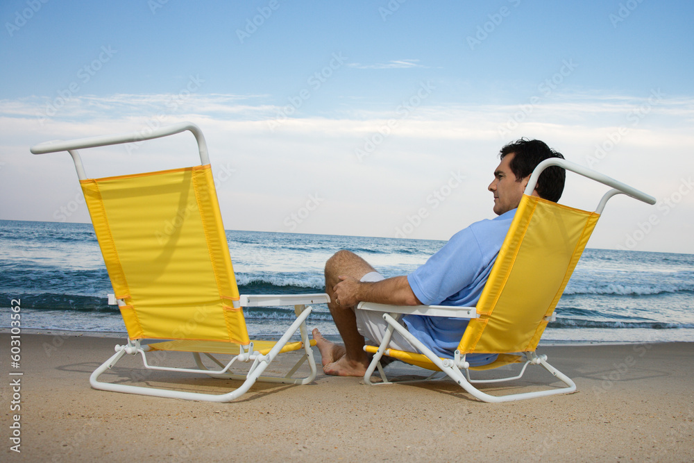 Man sits on the beach alone and looks at an empty chair. Horizontal shot.