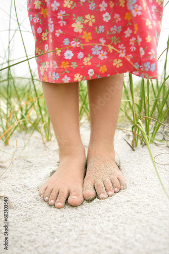 Closeup of a little girl's barefoot feet that are covered in sand. Vertical shot.