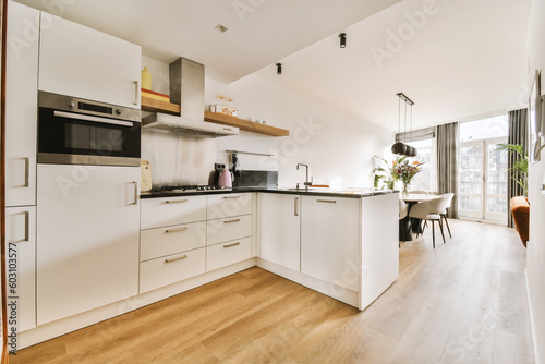 a kitchen and dining area in a house with wood flooring, white cupboards and appliances on the wall