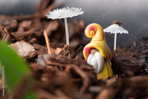 A small, yellow clad, gnome among a single, tiny, clear-white mushroom in focus with a larger, similar mushroom out of focus.  Nature background, macro. photo